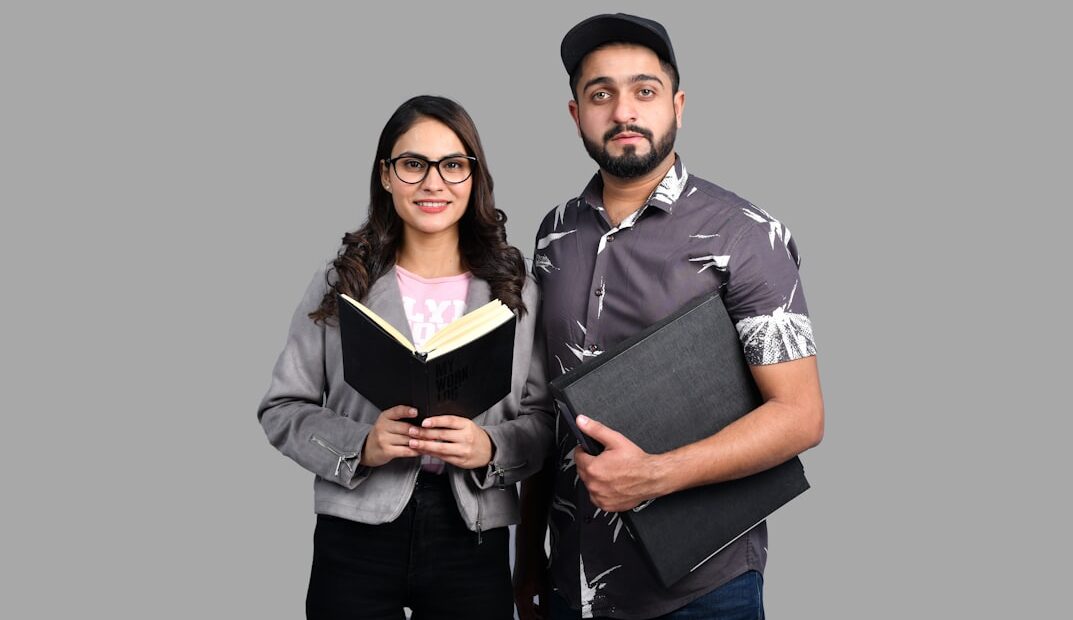 Ein Mann und eine Frau halten Bücher in der Hand und schauen in die Kamera.