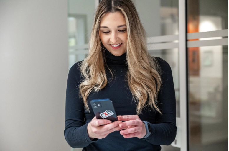 Eine Frau in schwarz gekleidet steht vor einem gläsernen Büro und hält ein iPhone in der Hand. Sie schaut sich die Definition von der Mehrfachbeschäftigung an.