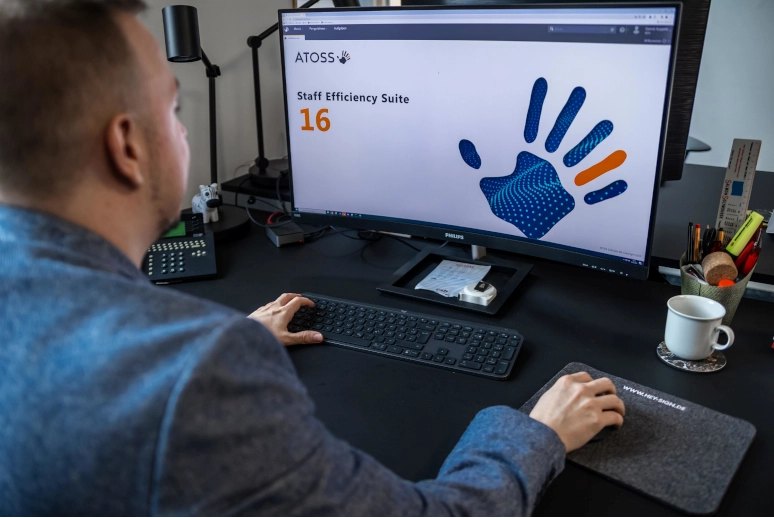 Ein Mann sitzt vor einem PC auf dem gerade ATOSS gestartet wird, um sich mit Workforce Analytics zu befassen.