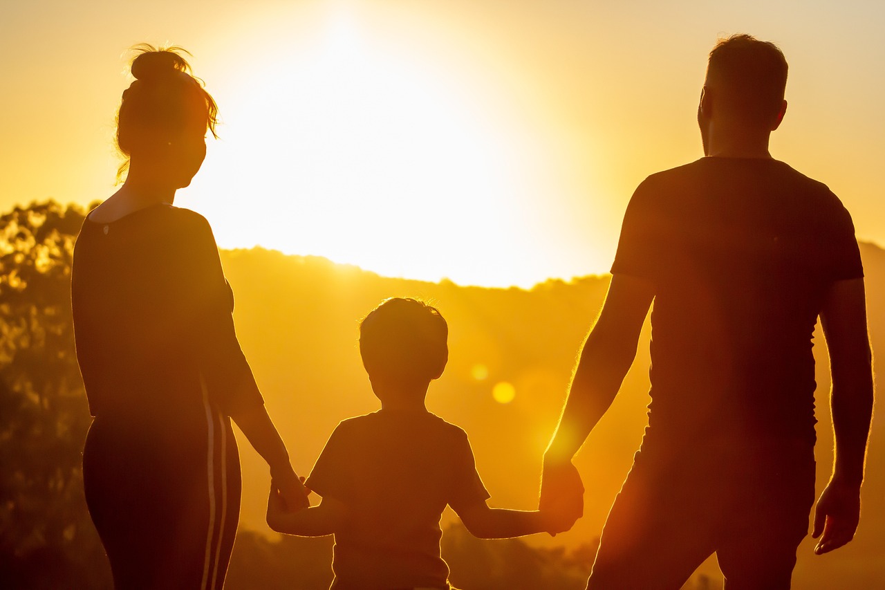 Eine Frau, ein Mann und ein Kind gehen Hand in Hand auf offenem Feld Richtung Sonnenuntergang. Möglich durch Ferienbetreuung