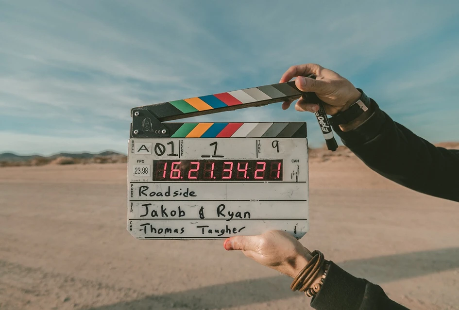 Eine Filmklappe wird vor die Kamera gehalten, Hintergrund ist wüstenhaft, die Klappe ist mit Roadside Jakob und Ryan beschriftet. Führung durch Filme