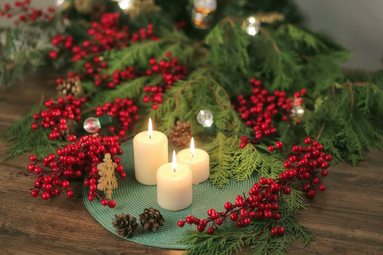 Ein Adventskranz mit weißen Kerzen und roten Verzierungen steht auf einem dunkelbraunen Holztisch. Ein Krankbindekurs als Teambuilding an Weihnachten.