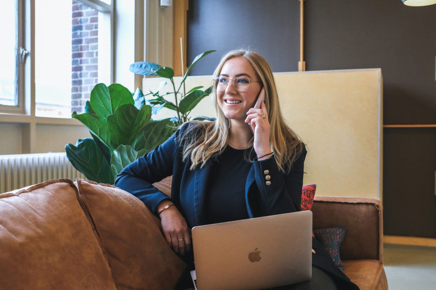 Freelancer-Boom: Wie HR diesen Trend meistern und von ihm profitieren kann, dargestellt durch eine blonde Frau die auf einem Sofa sitzt. mit einem Laptop und telefoniert.