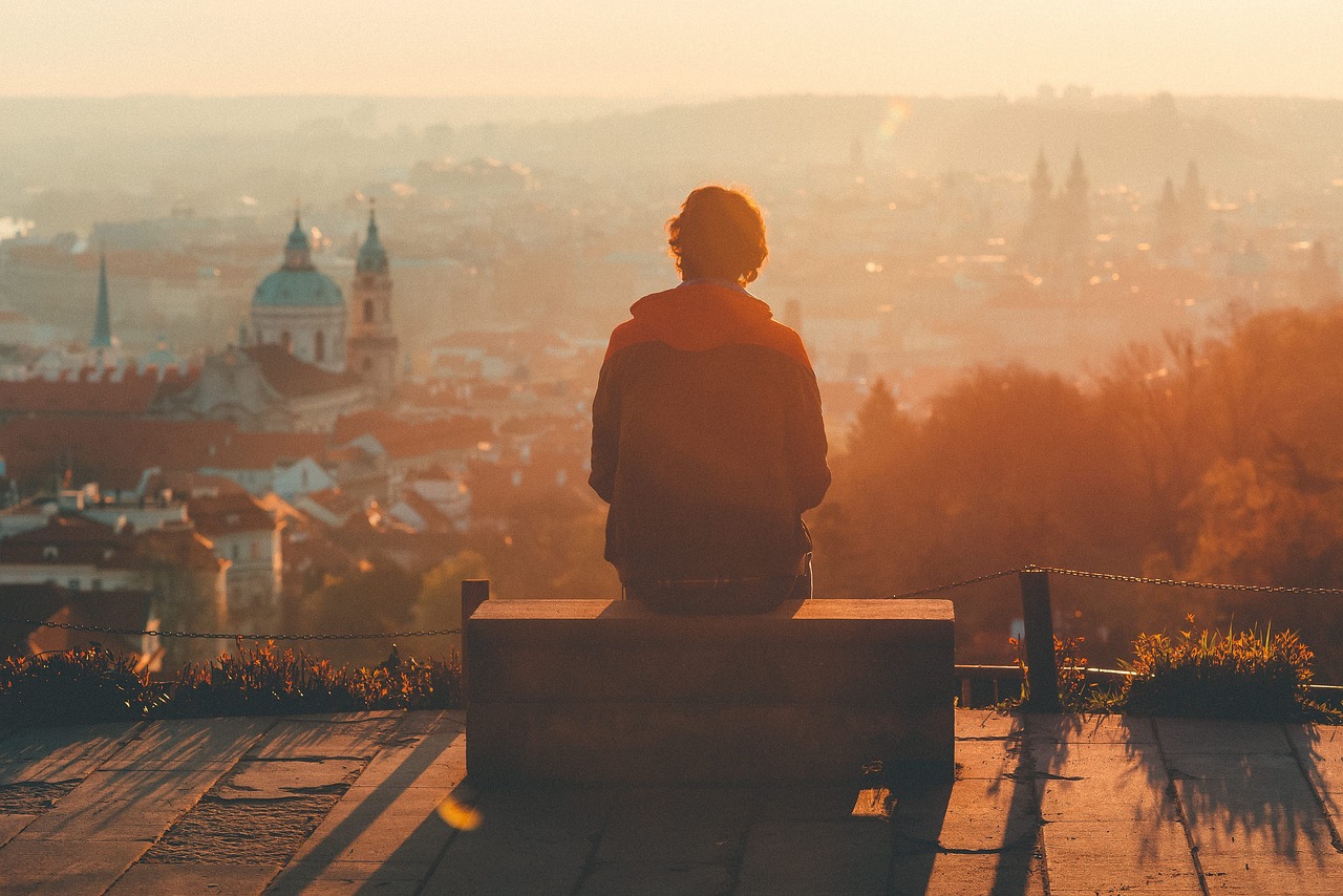 Mann auf einer Bank betrachtet Sonnenuntergang über einer Stadt. Symbolisch für die Loneliness Awareness Week