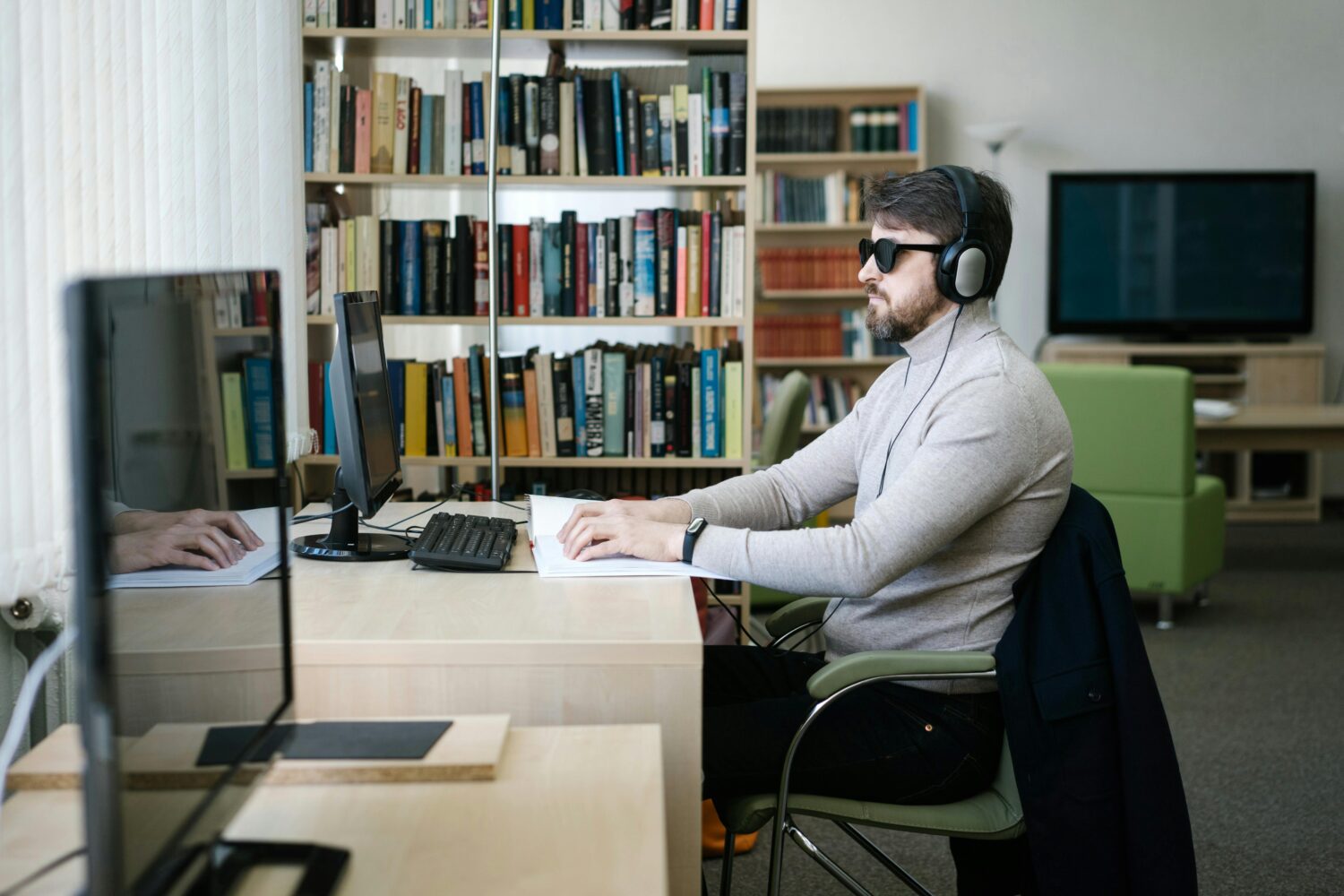 Sehbehinderter Mann sitzt vor Computer mit Kopfhörern und Brille.