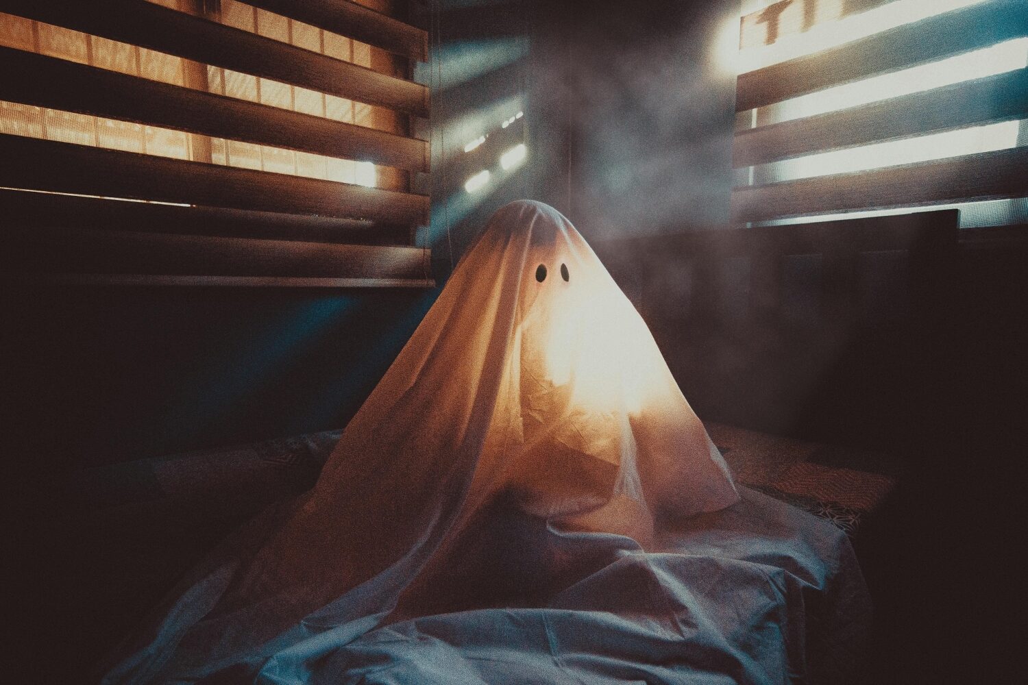 Geist sitzt auf einem Bett in einem abgedunkelten Zimmer.