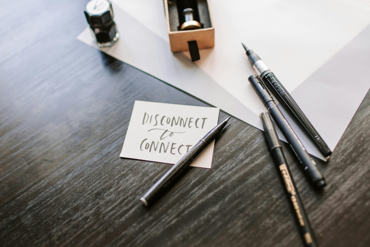 Auf einem Tisch liegt ein Zettel, auf dem steht: disconnected to connect, daneben liegen Kugelschreiber, es soll ein symbol für ein wertschätzendes Offboarding sein