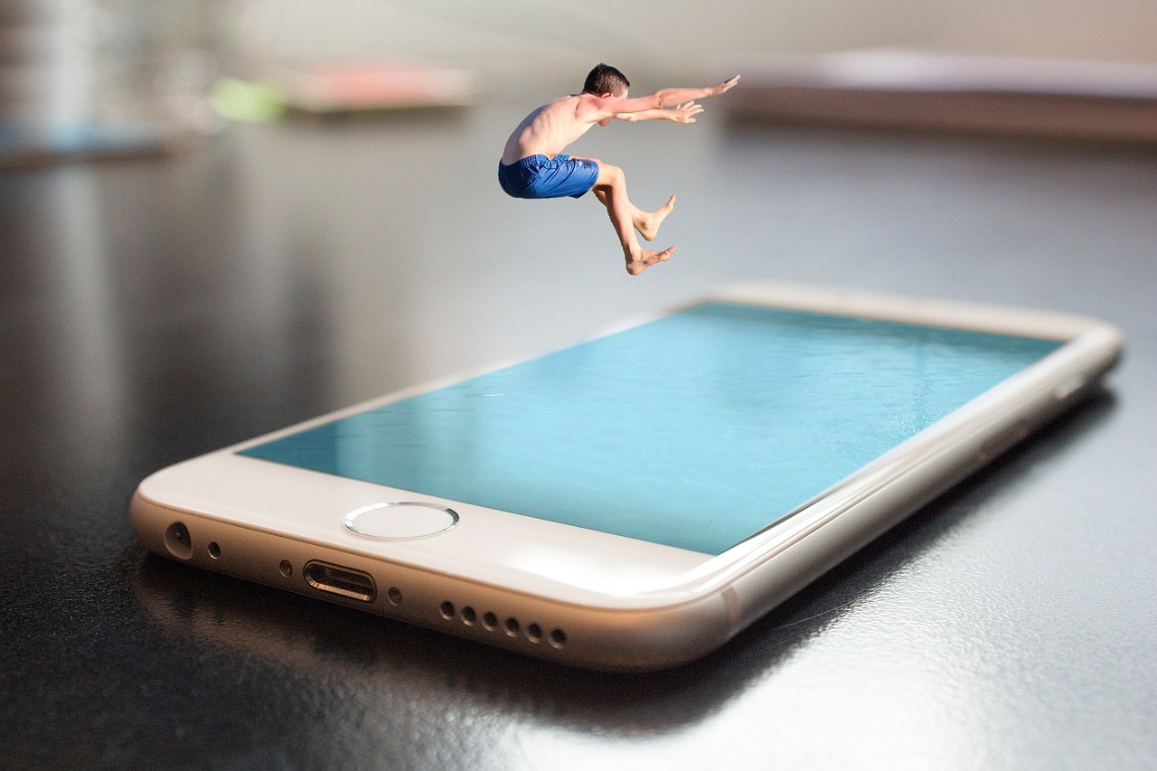 Ein Handy liegt auf einer Fläche, das Display sieht aus wie Wasser und ein kleiner Mensch spring gerade dort rein.