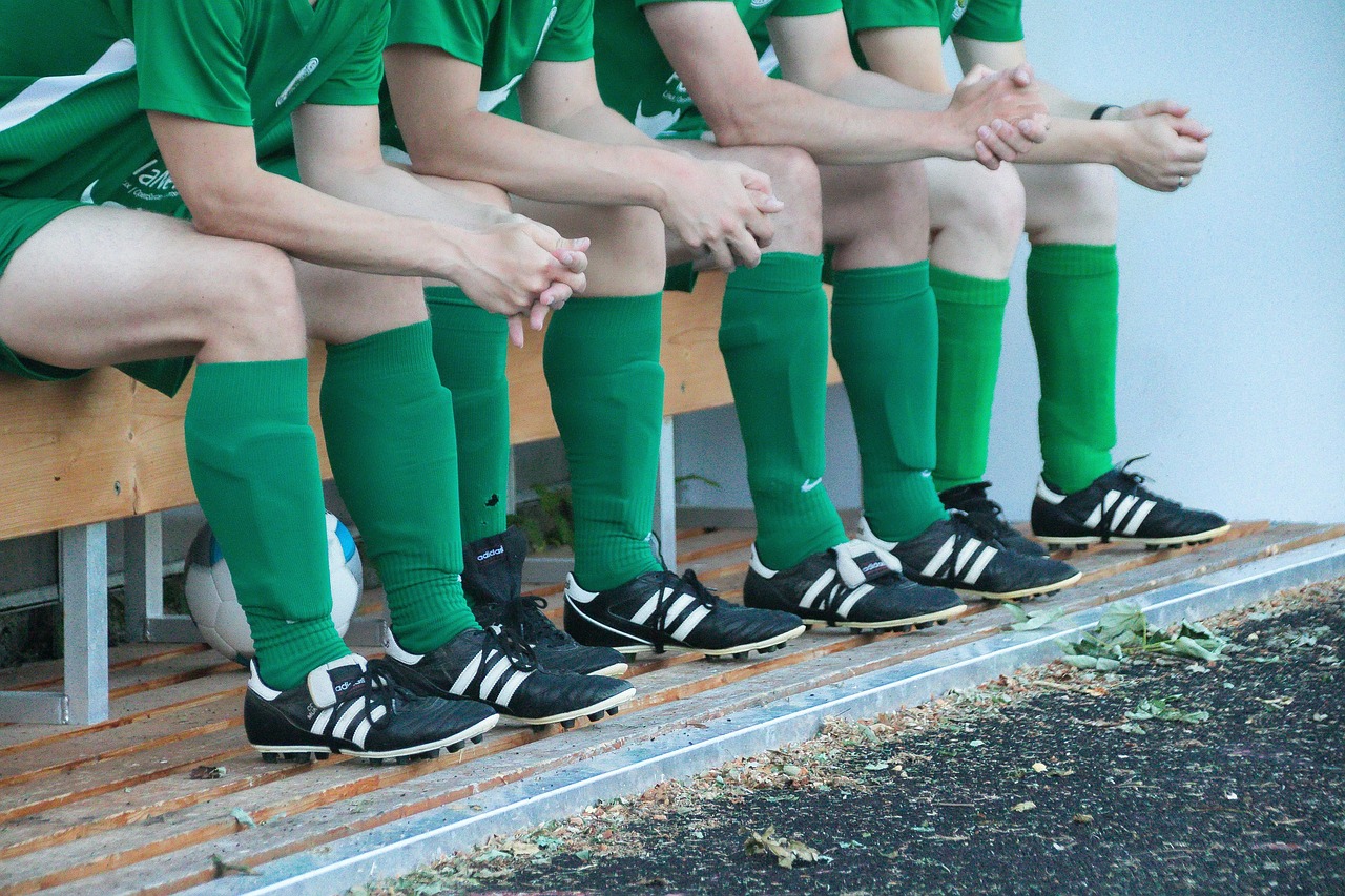 Ersatzspieler im grünen Trikot sitzen auf einer Ersatzbank beim Fußballspiel.